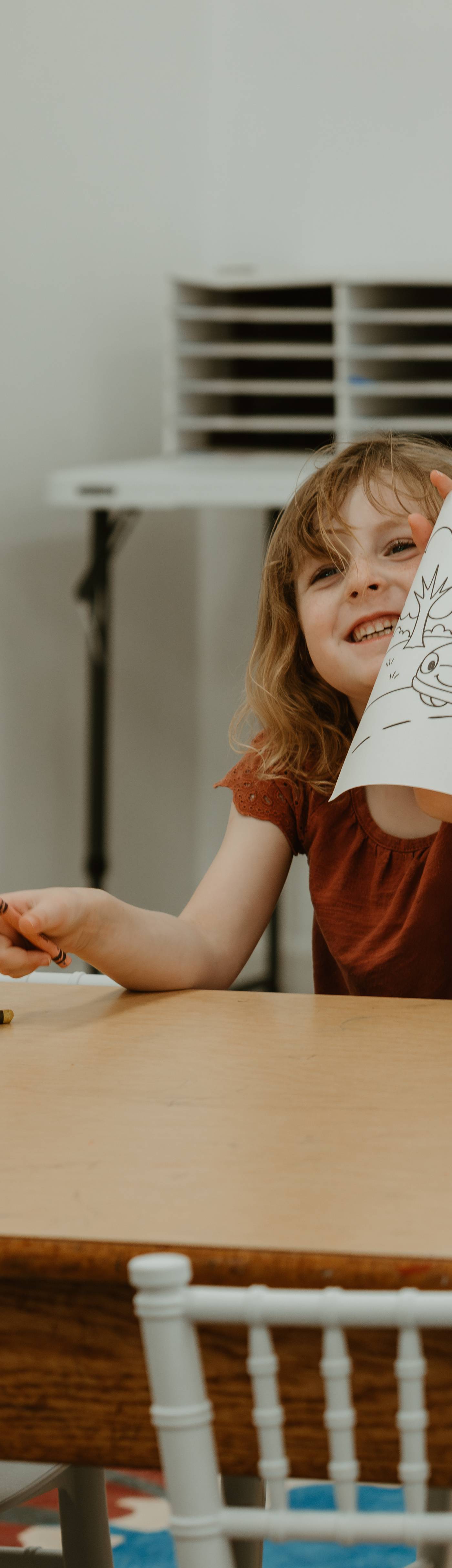 A child showing off a coloring page at a party table at Catalillies Play Café